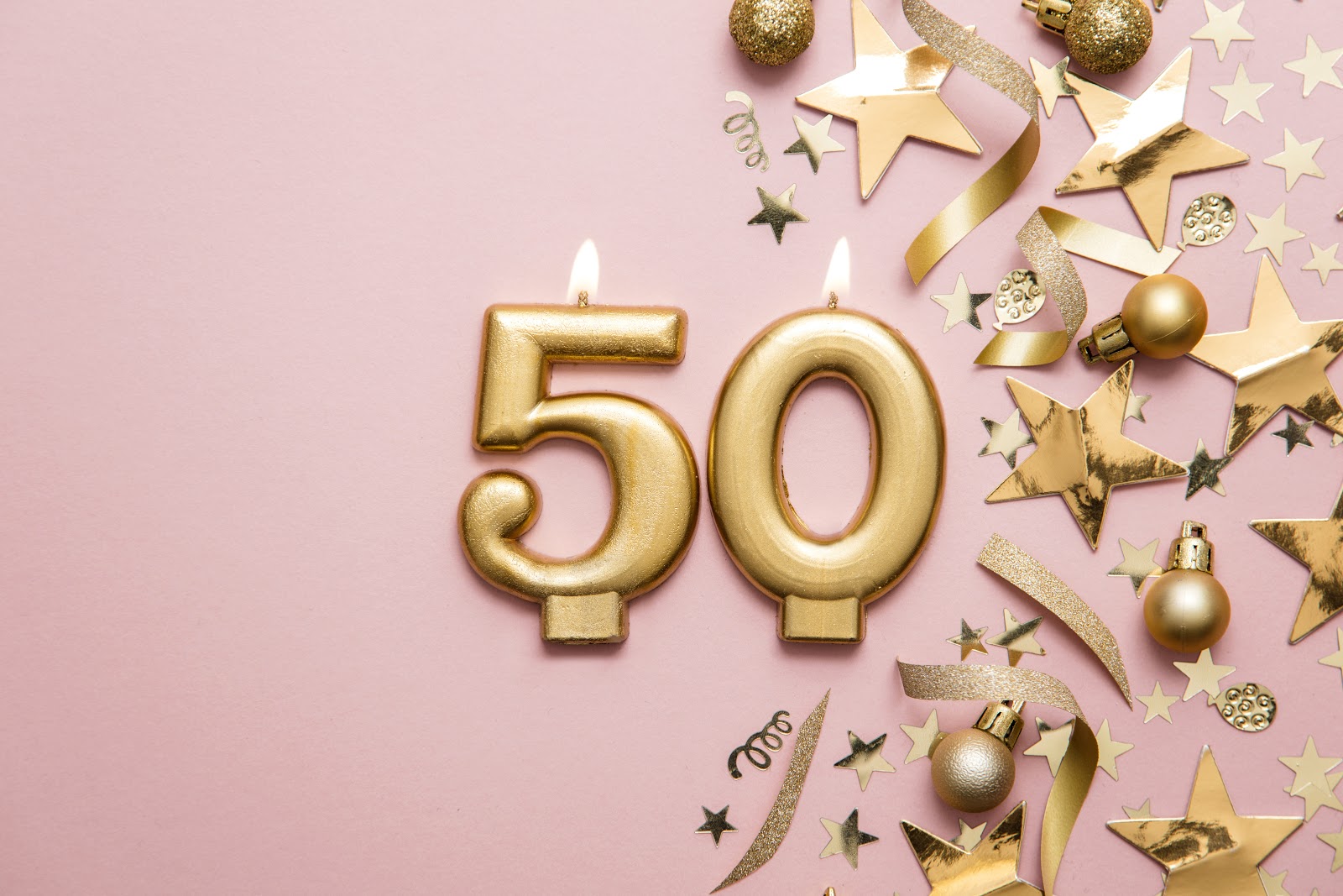 50 歲生日派對創意:50 號金蠟燭,旁邊有金色五彩紙屑和小玩意,粉紅色背景