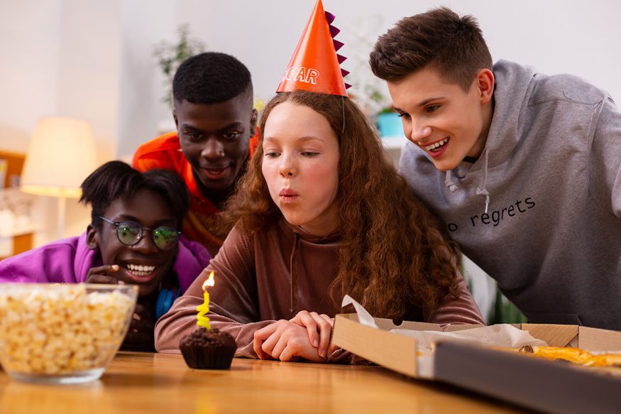 青少年生日派對創意:女孩在派對上被朋友包圍時吹蠟燭