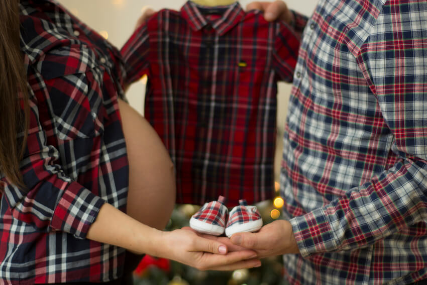 聖誕節懷孕公告:丈夫和一名孕婦拿著嬰兒的衣服和鞋子